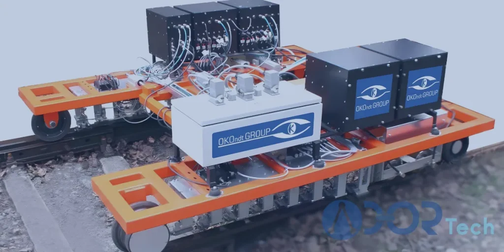 An eddy current rail inspection system mounted on an orange frame with multiple electronic modules and sensors used for non-destructive testing of railway tracks.