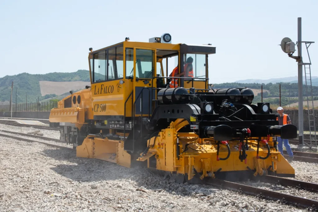 Yellow ballast regulator machine on railway tracks for ballast maintenance and track bed profiling