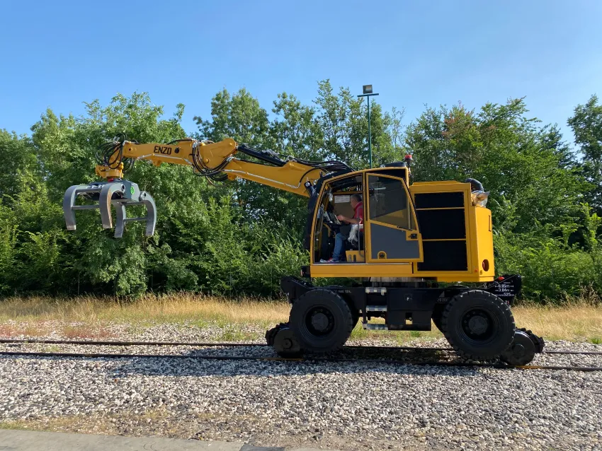 Rail excavator with grapple attachment on railway tracks for maintenance work.