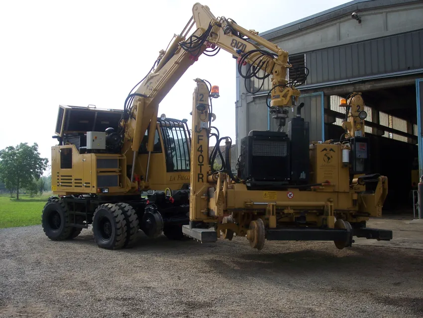 Hi rail excavator lifting railway maintenance equipment with road-rail capability.