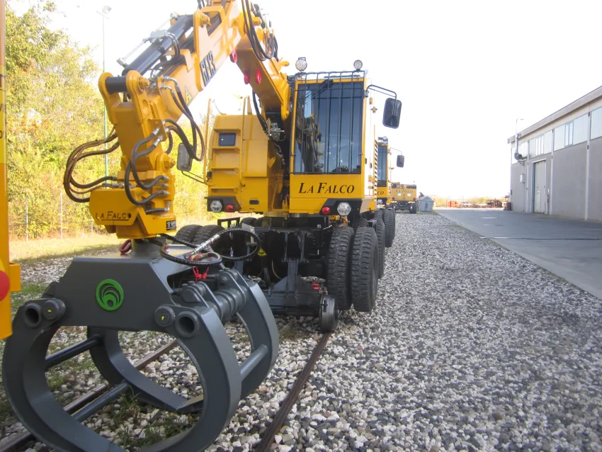 Road rail excavator with grapple attachment on railway tracks for maintenance work.