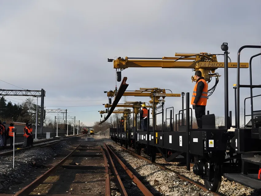 Train loader with rails loader cranes carrying long rail sections for railway track construction.